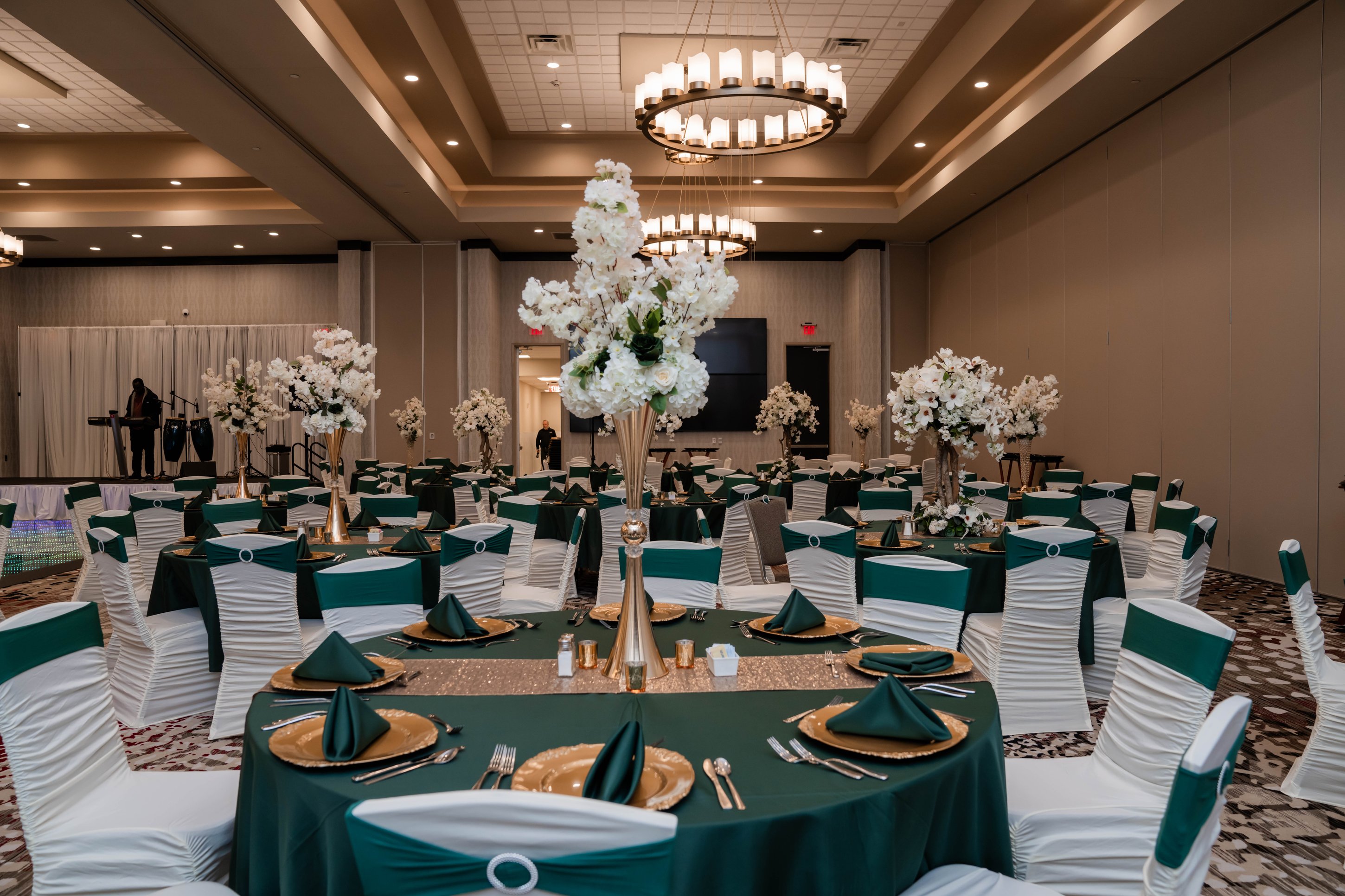 Teal and gold table settings with white chair covers and floral centerpieces at event venue